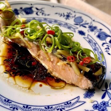 Side shot of Chinese steamed salmon fish in a soy based sauce with spring onions.