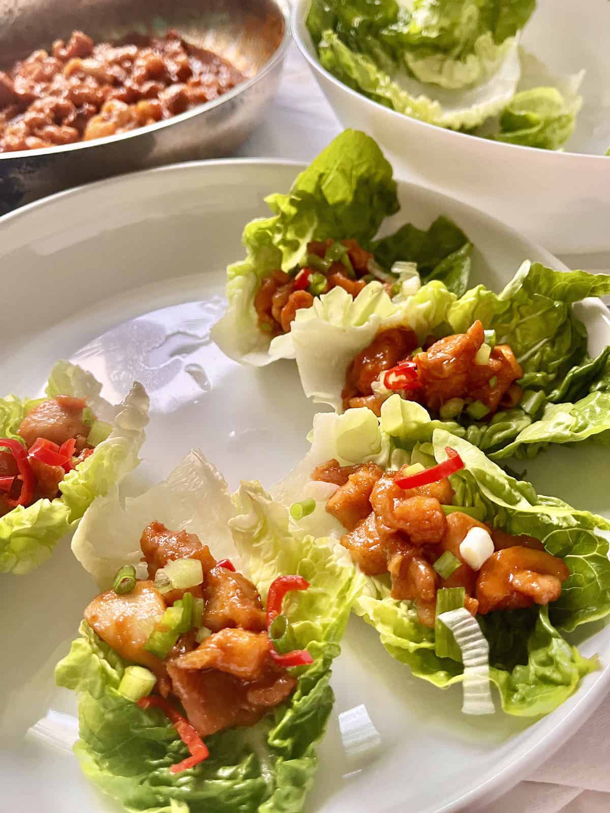 Gochujang chicken in lettuce cups on a white plate.