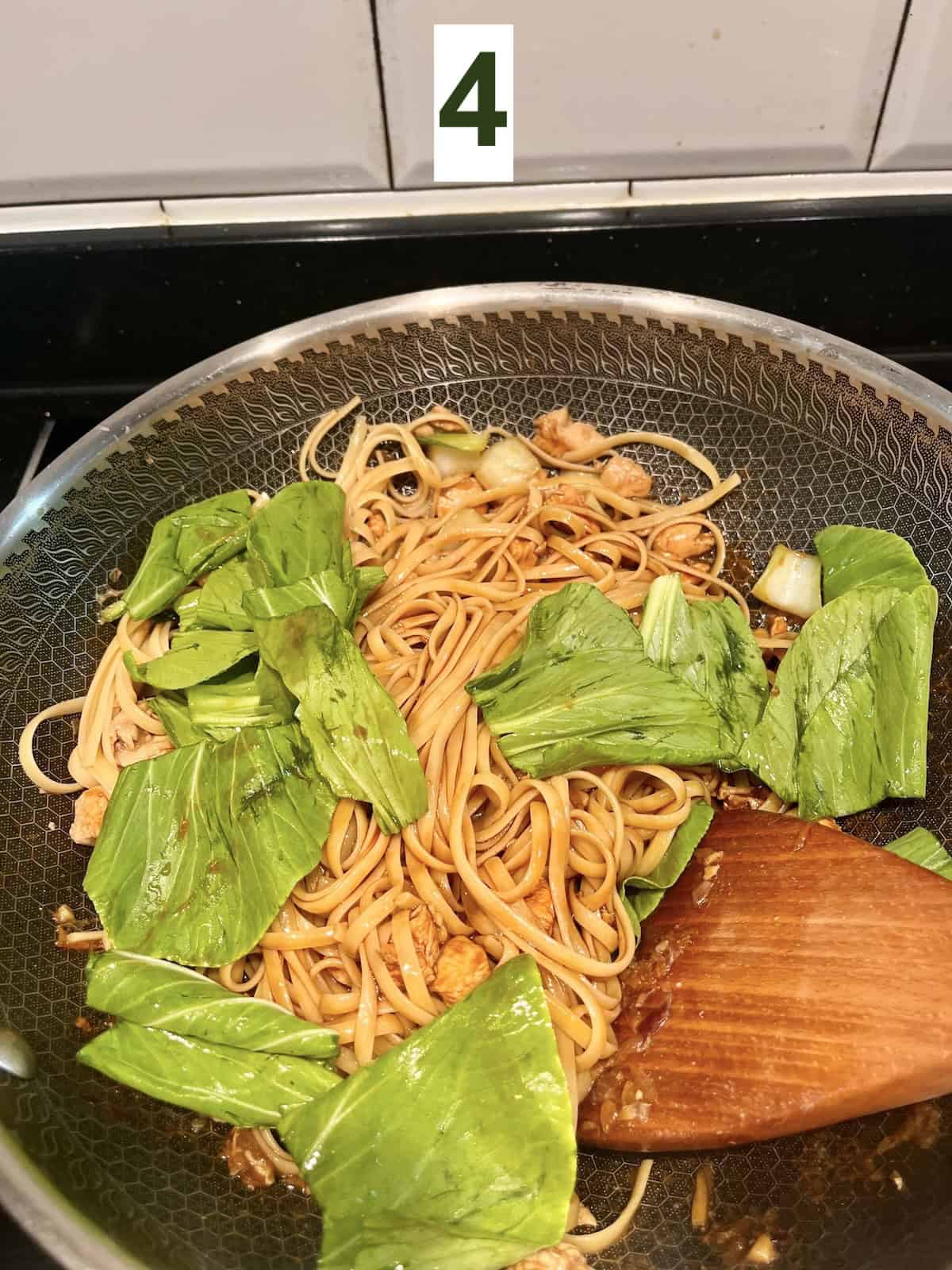 Adding green veggie leaves to chicken lo mein spaghetti noodles.