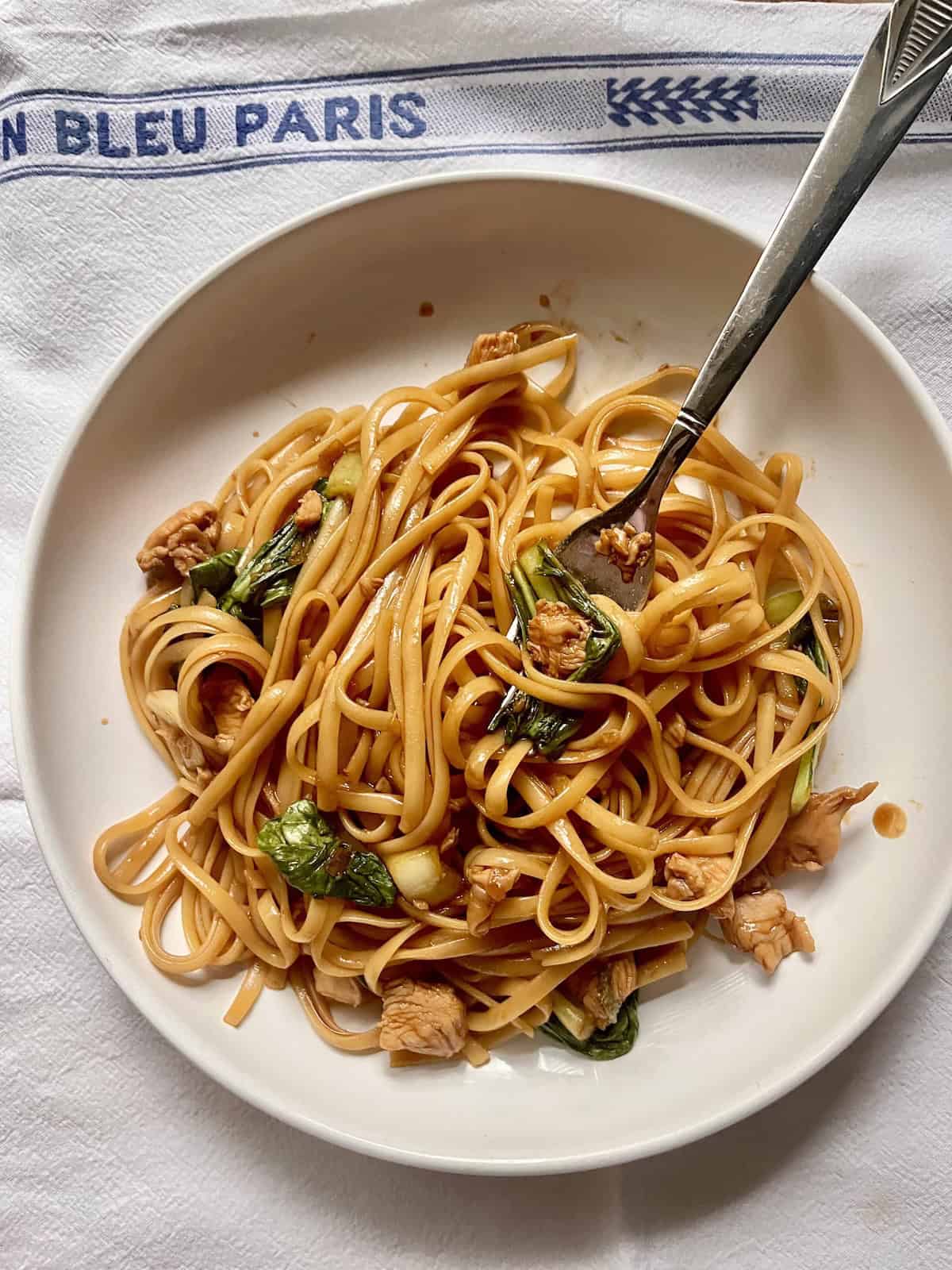 Using a fork to pick up chicken lo mein spaghetti noodles and bok choy.