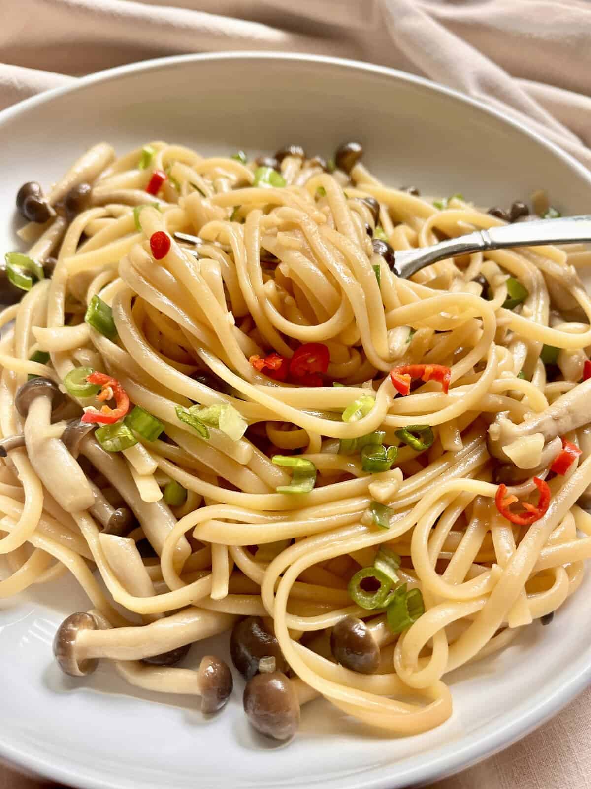 Garlic butter noodles Chinese spaghetti with mushrooms on a white plate.