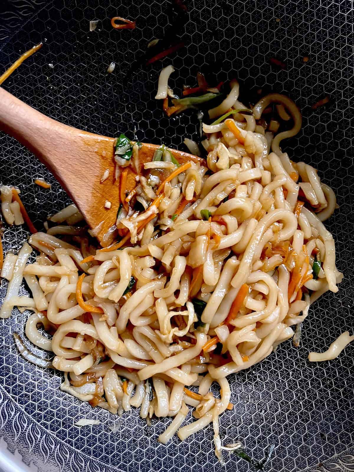 Stir frying udon noodles in a wok.