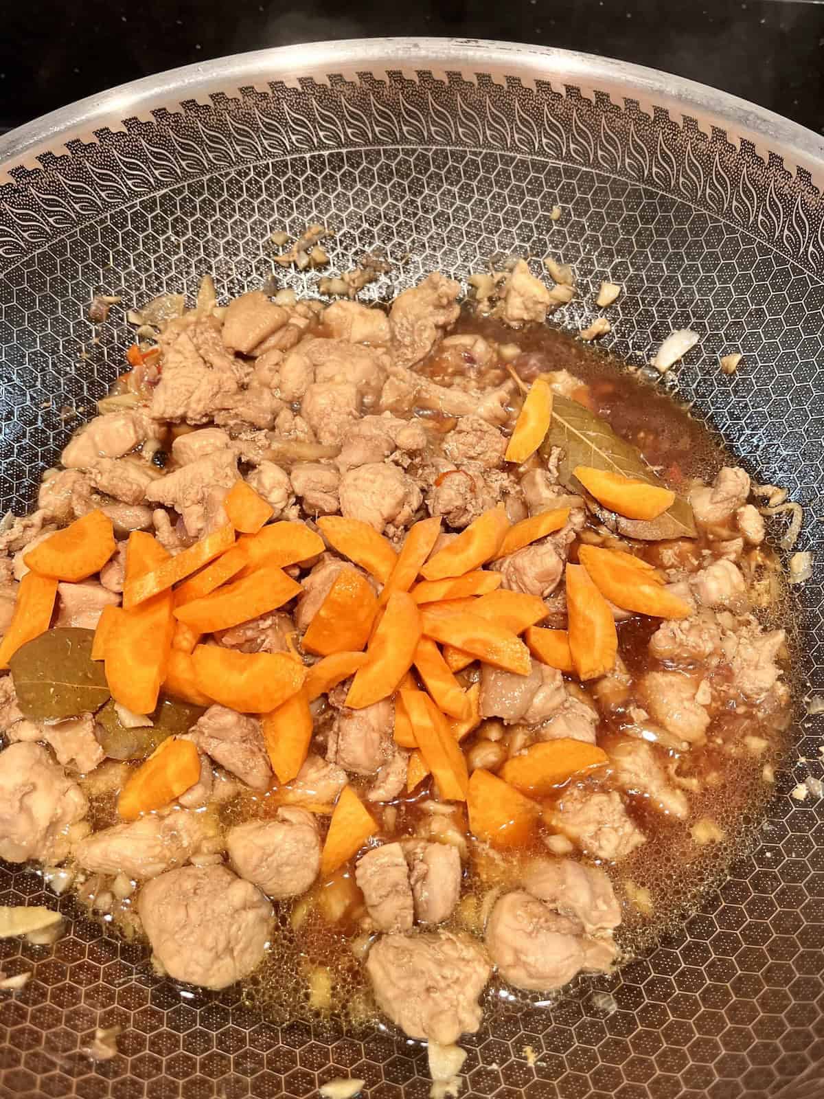 Carrots in a wok of Filipino adobo with chicken thighs.