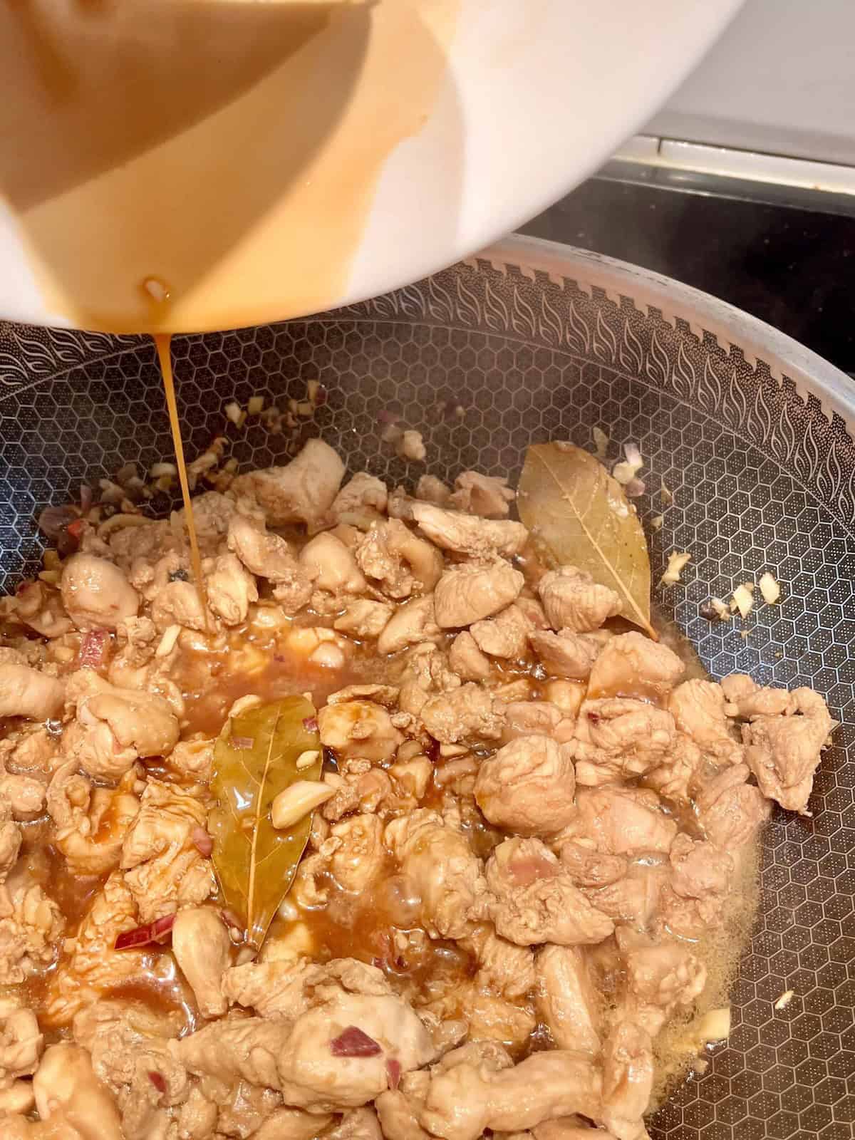 Adding adobo marinade to a wok.