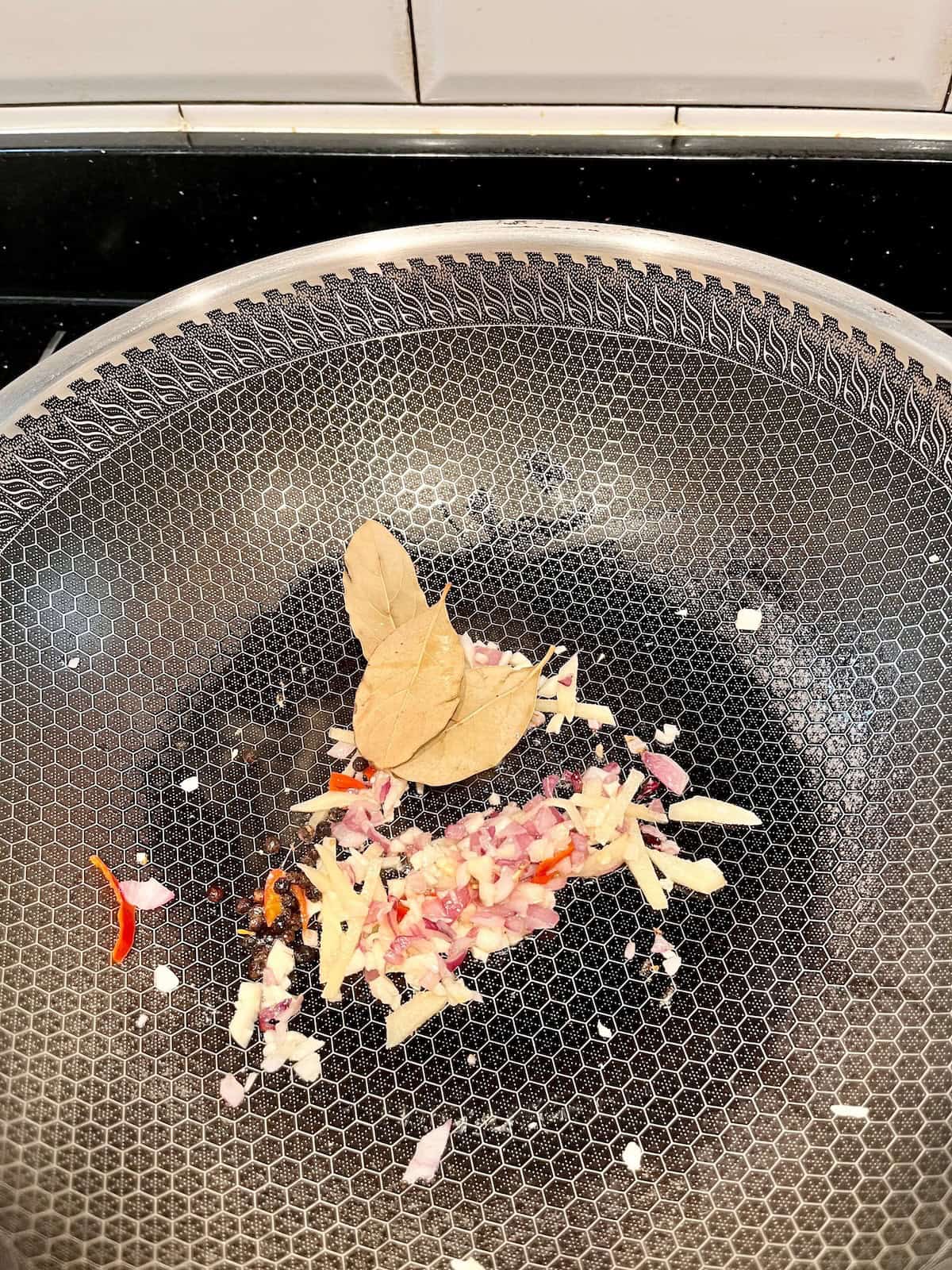 Sautéing ginger, garlic, onions, and bay leaves in a wok.