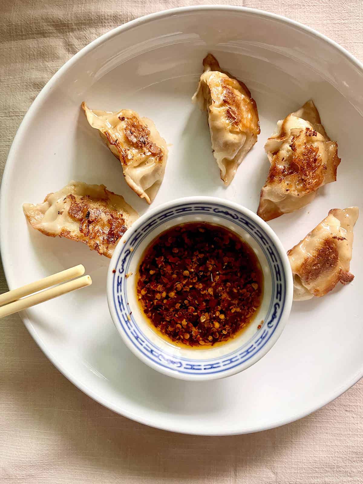 Japanese gyoza dumplings and sauce on a white plate.