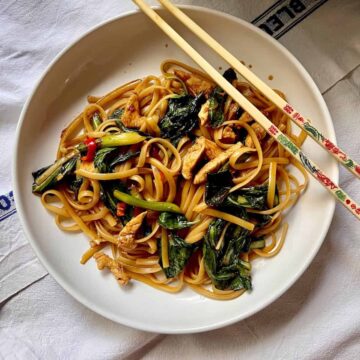 Thai noodles with green vegetables on a white plate.