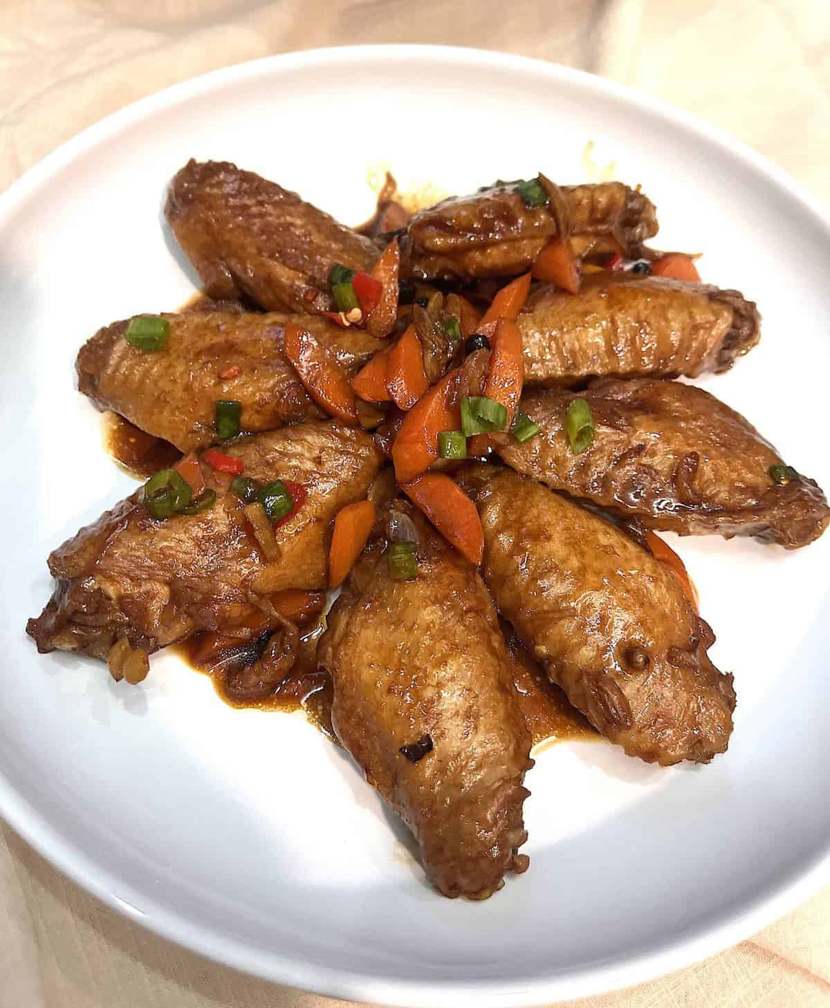 Braised chicken wings and carrots in adobo sauce on a white plate.