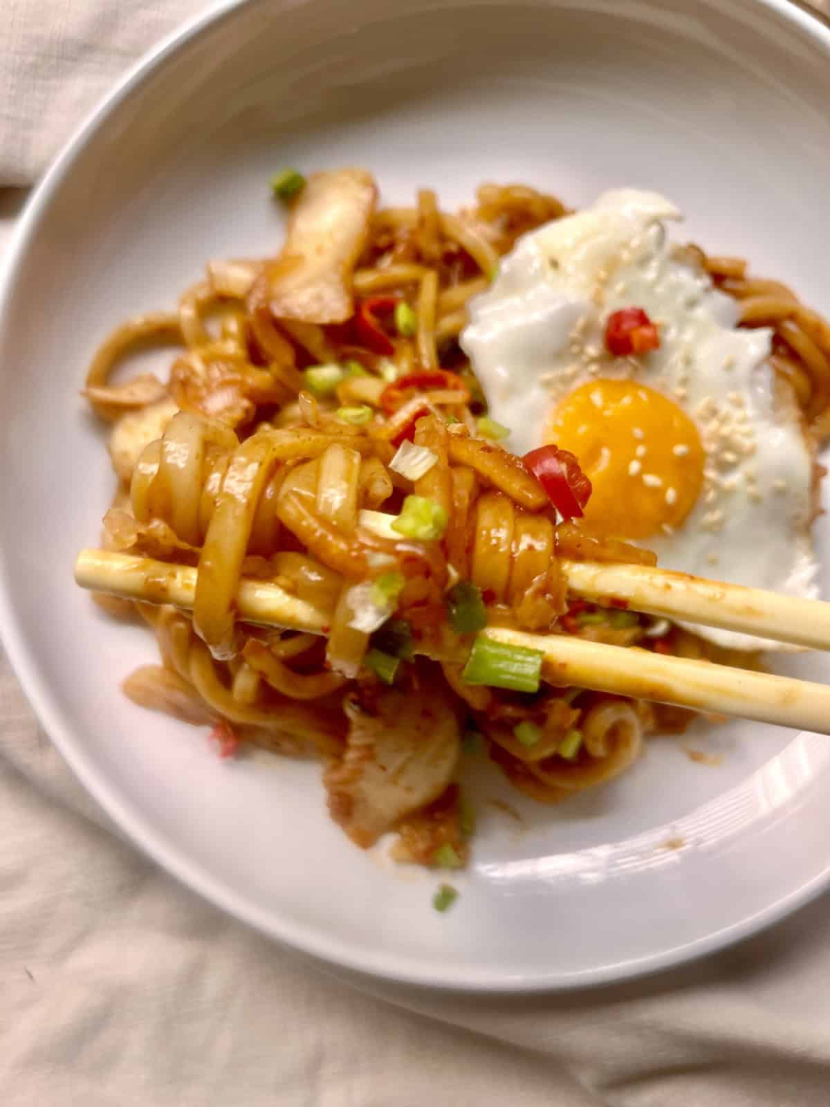 Picking up udon noodles from a plate of kimchi udon and egg.