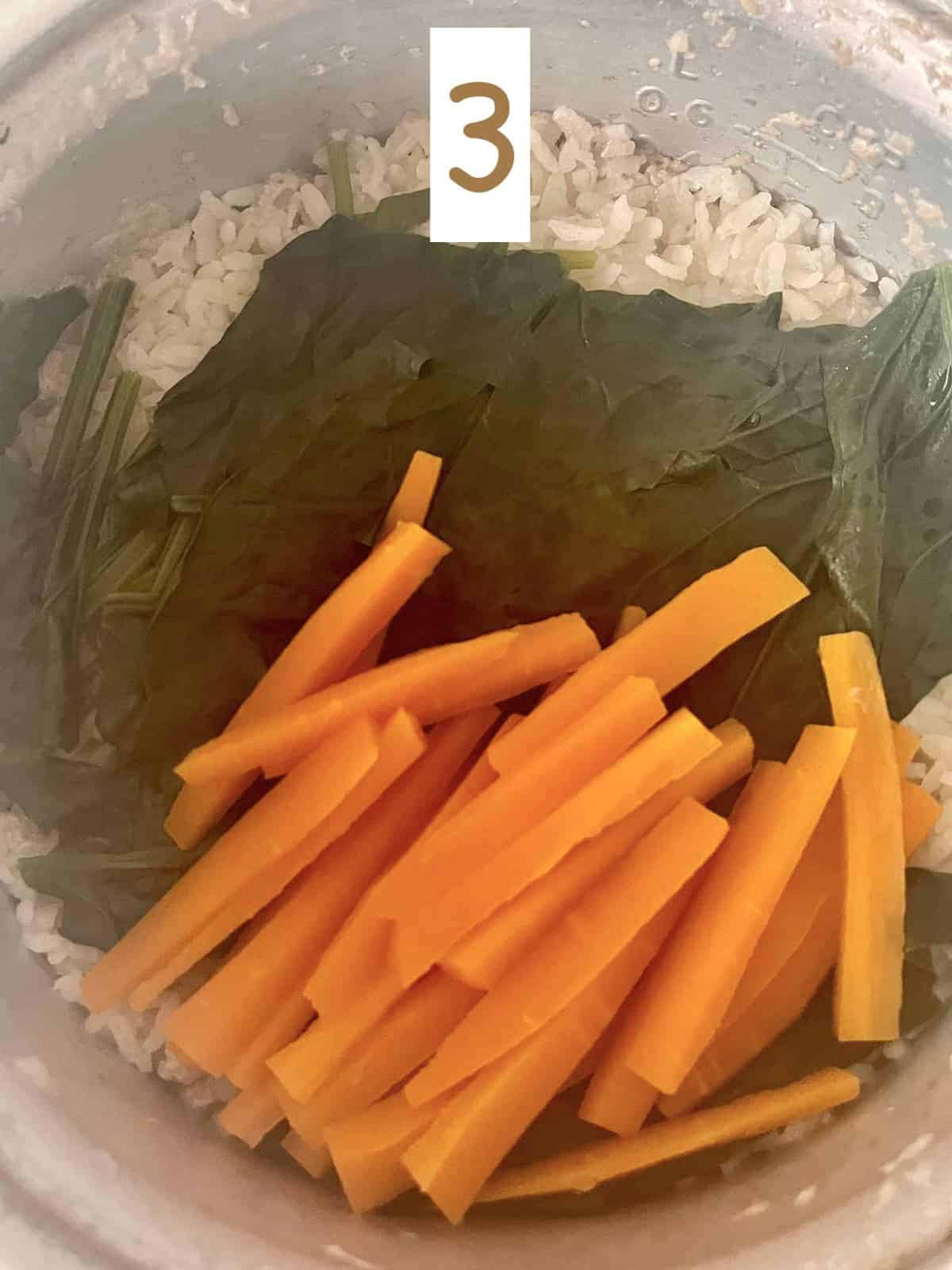 Cooked spinach and carrots and rice in rice cooker pot.