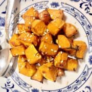 Baked butternut squash cubes on a white and blue plate.